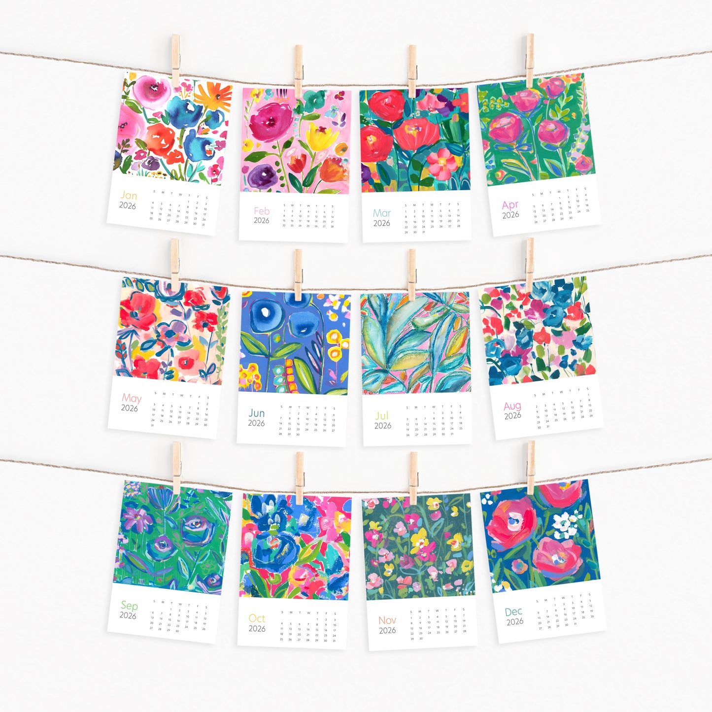Colorful floral calendar pages by Melissa Doty hanging on a line with wooden clips.