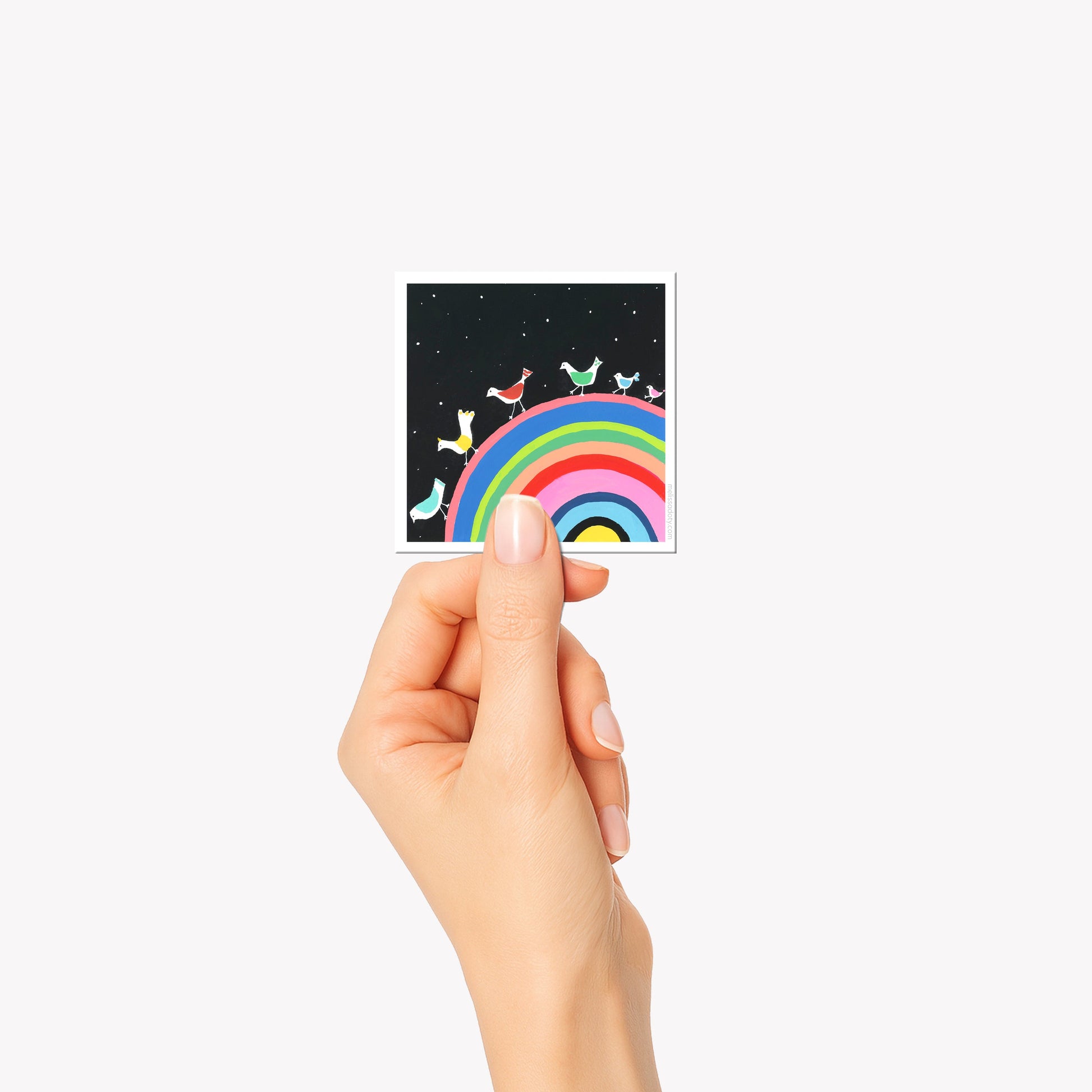Hand holding a small card with a rainbow design on a white background