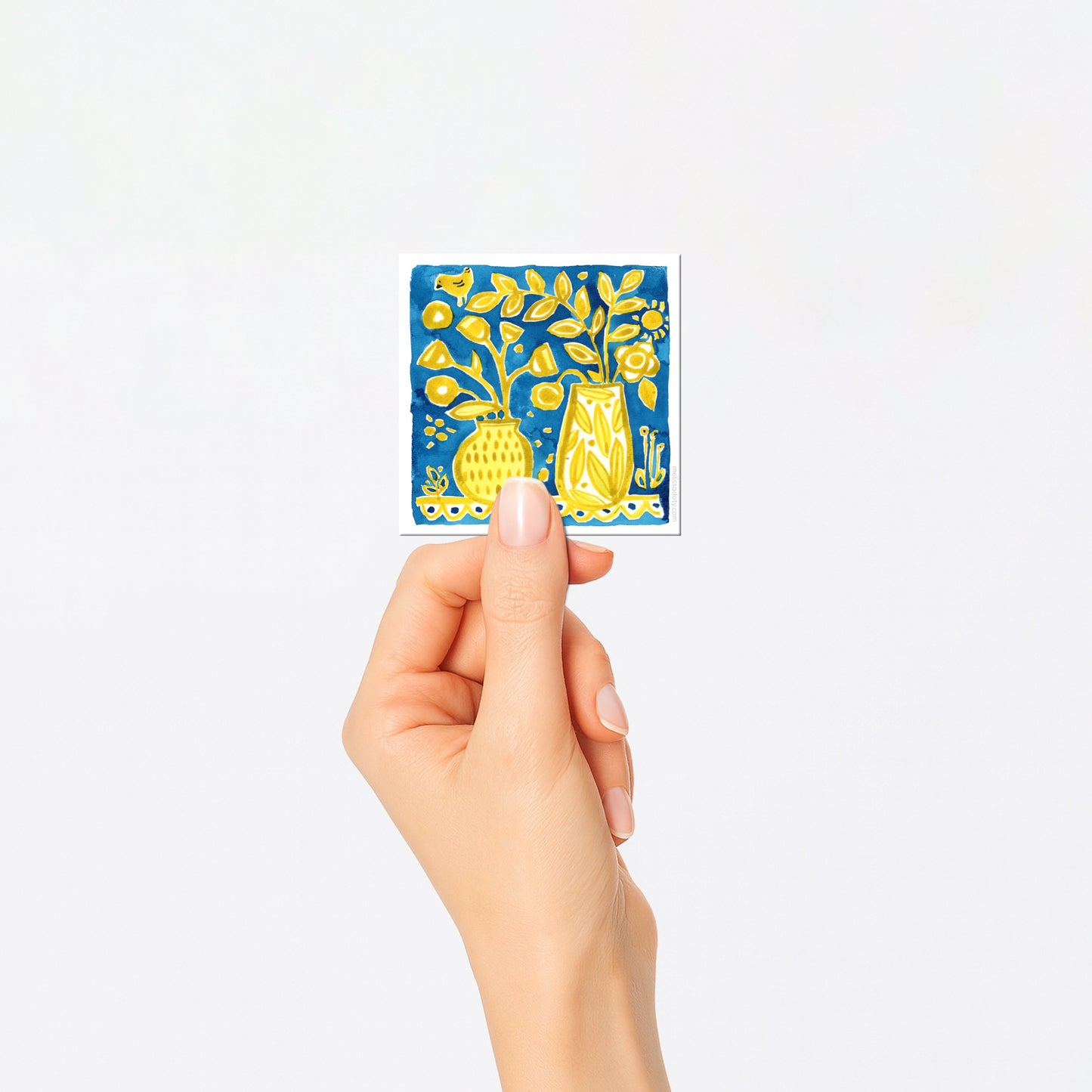 Hand holding a small card with floral design on a white background