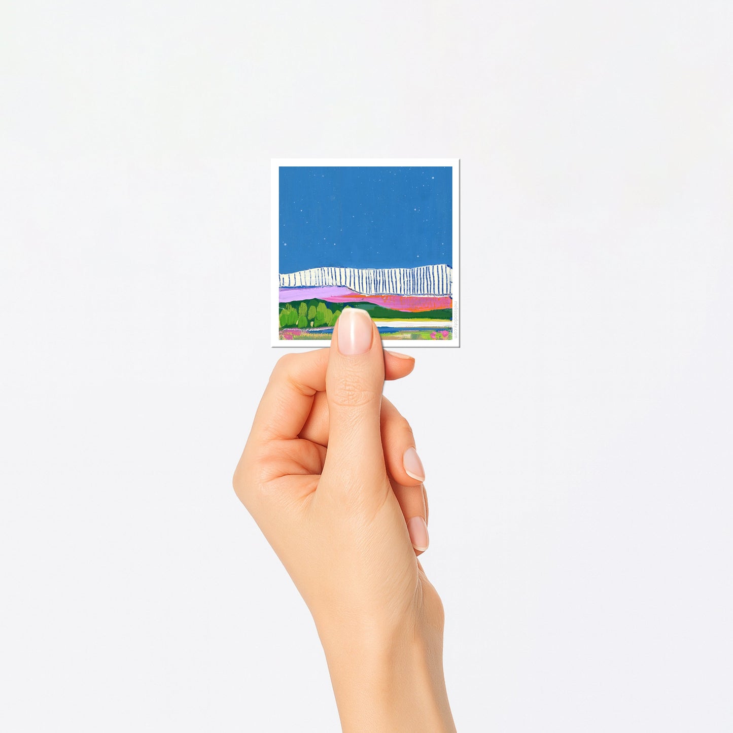 Hand holding a small rectangular card with a colorful landscape design on a white background