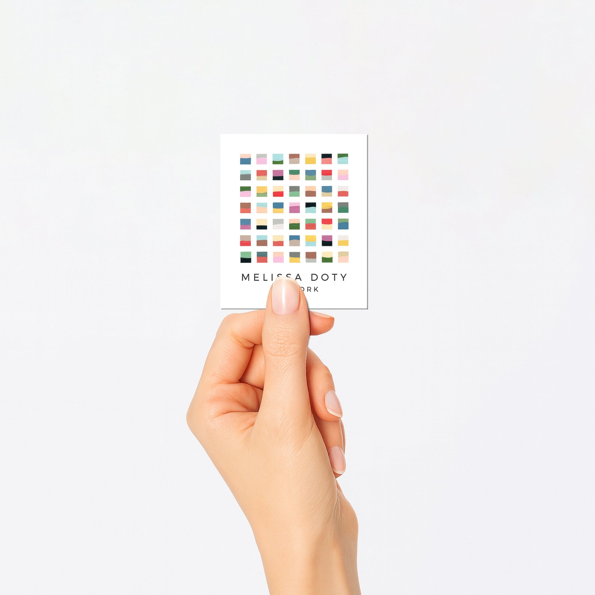 Hand holding a small card with colorful dots and text on a white background